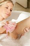 Jeune femme en frottant sa jambe avec une éponge de bain dans une baignoire