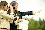 Teenage girl pointing forward with a girl looking through a pair of binoculars