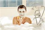 Portrait d'une jeune femme avec un masque facial tenant une éponge de bain dans une baignoire