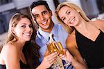 Two young women and a mid adult man toasting with champagne flutes