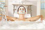 Nahaufnahme einer jungen Frau mit einer Gesichtsmaske, die Entspannung in der Badewanne