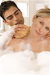 Close-up of a young man scrubbing a young woman's neck with a bath sponge