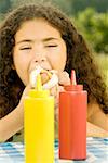 Close-up of a girl eating a burger behind sauce bottles