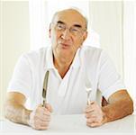Portrait d'un homme senior tenant une fourche avec un couteau de table