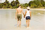 Rear view of a young man and a teenage girl holding hands walking on the beach