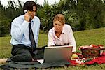 Businessman and a businesswoman sitting in front of a laptop in the park