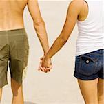 Mid section view of a young man and a teenage girl holding hands on the beach