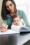 Mutter schreiben im Notizbuch mit Baby auf dem Schoß