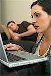 Woman Working at Computer and Man Napping on Couch