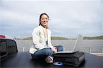 Woman Sitting on Back of Truck Using Laptop