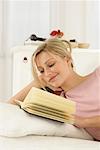 Woman lying on bed, reading a book