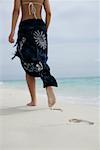 Young girl walking at the beach, footprints in the sand, rear view