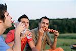 Three young men eating and drinking