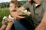 Father and son sitting on meadow while they eat sandwiches