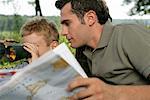 Father holding world map while his son is looking through binoculars