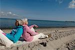Two mature women sitting back to back at Baltic Sea beach