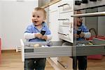 Baby boy standing next to a kitchen drawer and holding a mobile phone in his hands