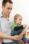 Father reading a journal, while son  sitting on his lap