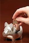 Human hand putting a single Euro into a piggybank, close-up