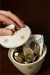 Hand holding the top of a sugar bowl filled with Euro bills (part of), close-up