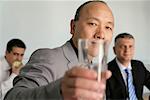 Asian businessman holding a glass at camera, two persons sitting in background