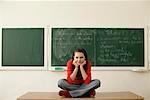 Teenage girl sitting on a table, blackboard in background