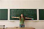 Teenage girl with outstretched arms standing in front of a blackboard