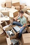 Man Sitting amongst Moving Boxes with Laptop Computer