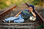 Boy With Soccer Ball Lying Down In Train Tracks