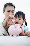 Girl Putting Money in Piggy Bank with Father