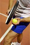 Low section view of a man holding a tennis ball and a tennis racket