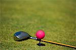 Close-up of a golf ball on a tee with a golf club on the grass