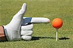 Close-up of a person's hand pointing at a golf ball on a golf tee