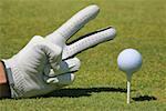 Close-up of a person's hand showing two fingers next to a golf ball on a tee
