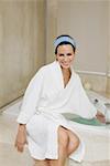 Portrait of a young woman sitting near a bathtub and checking the water temperature