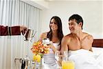 Person's hand serving tea to a young woman and a mid adult man on the bed