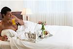 Jeune homme couché sur le lit, tenant un verre de jus d'orange