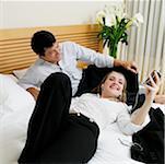 High angle view of a mid adult man lying on the bed with a young woman listening to an MP3 player