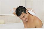 Jeune homme, frottant son dos avec un loofah dans la baignoire