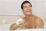 Close-up of a young man holding a loofah in a bathtub