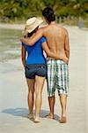 Rear view of a teenage girl walking on the beach with her arm around a young man