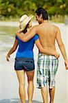 Rear view of a young man walking on the beach with his arm around a teenage girl