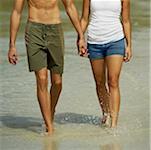 Mid section view of a young man and a teenage girl holding hands and walking on the beach