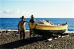 Rückansicht von zwei Männern in der Nähe ein Boot an einem Strand auf der Insel Martinique, Caribbean