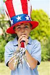 Porträt eines jungen großen Stars &amp; Stripes Hut trägt, bläst Noisemaker Horn