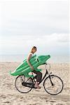 Woman Riding Bicycle and Carrying Inflatable Crocodile on Beach
