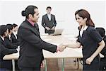 Side profile of a businessman and a businesswoman shaking hands in a meeting