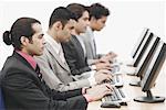 Side profile of four businessmen sitting in front of computers