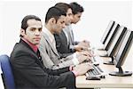 Profil latéral de quatre hommes d'affaires assis devant des ordinateurs