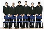 Portrait of a group of young men standing behind chairs holding mobile phones